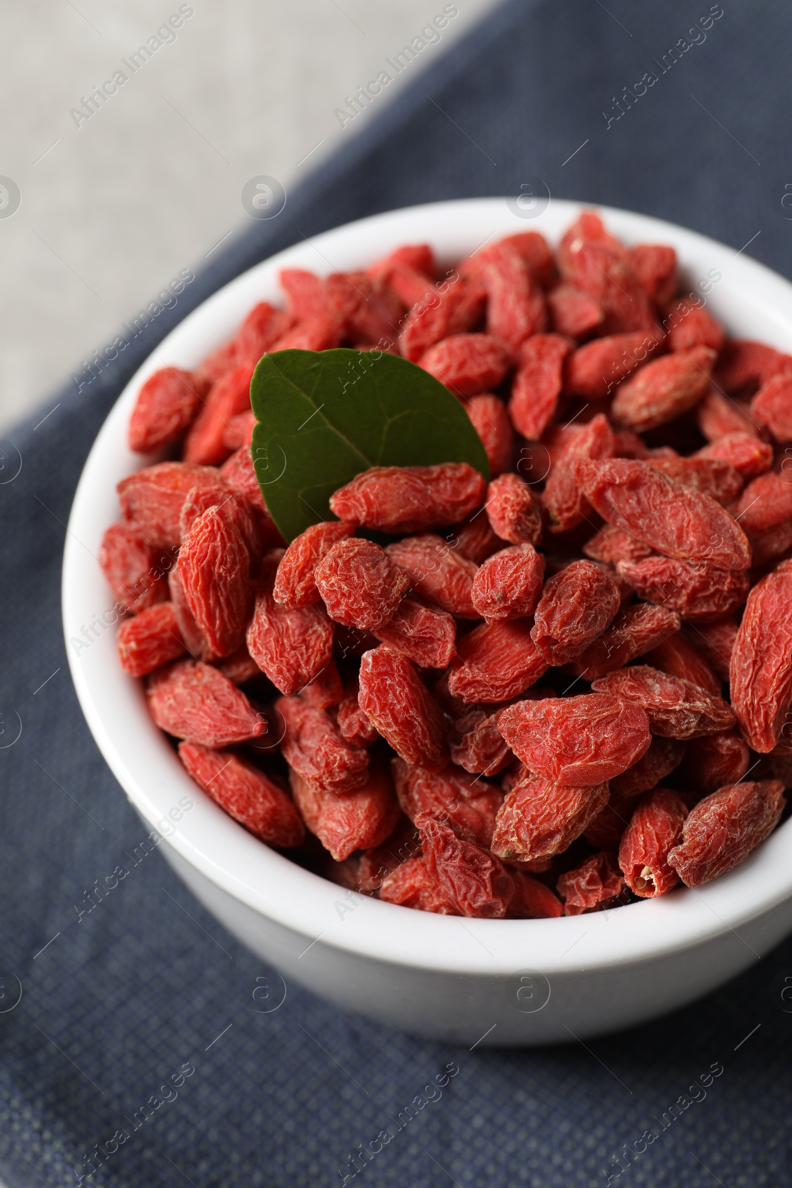 Photo of Dried goji berries in bowl on grey table, closeup