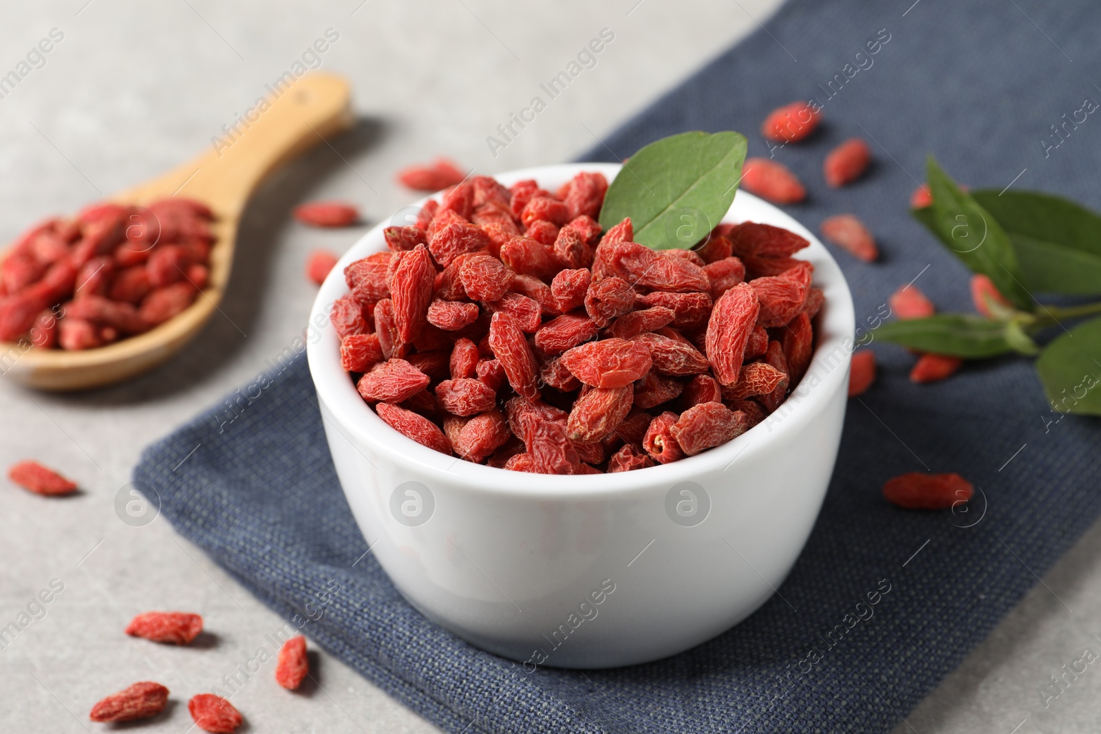 Photo of Dried goji berries and leaf in bowl on grey table, closeup
