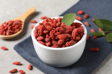 Dried goji berries and leaf in bowl on grey table, closeup