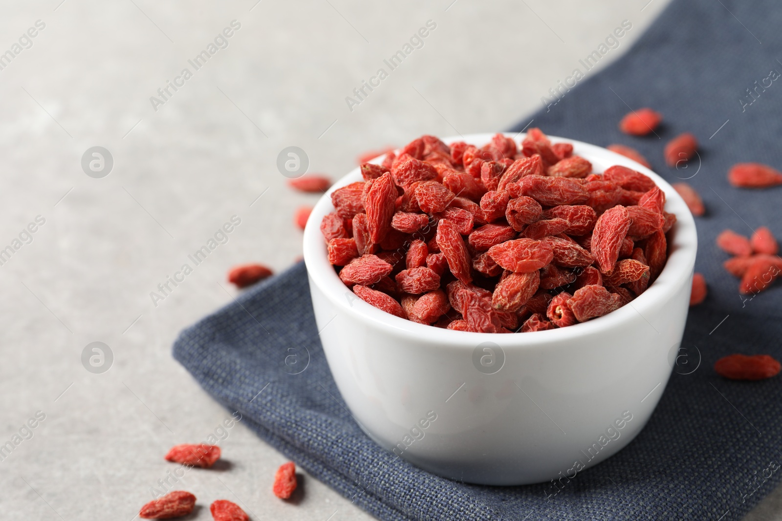 Photo of Dried goji berries in bowl on grey textured table, closeup. Space for text