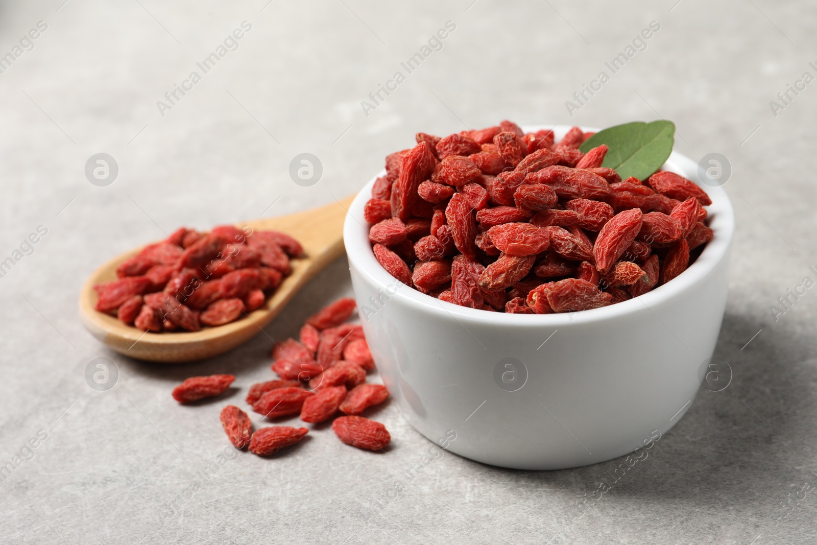 Photo of Dried goji berries in bowl and spoon on grey textured table, closeup
