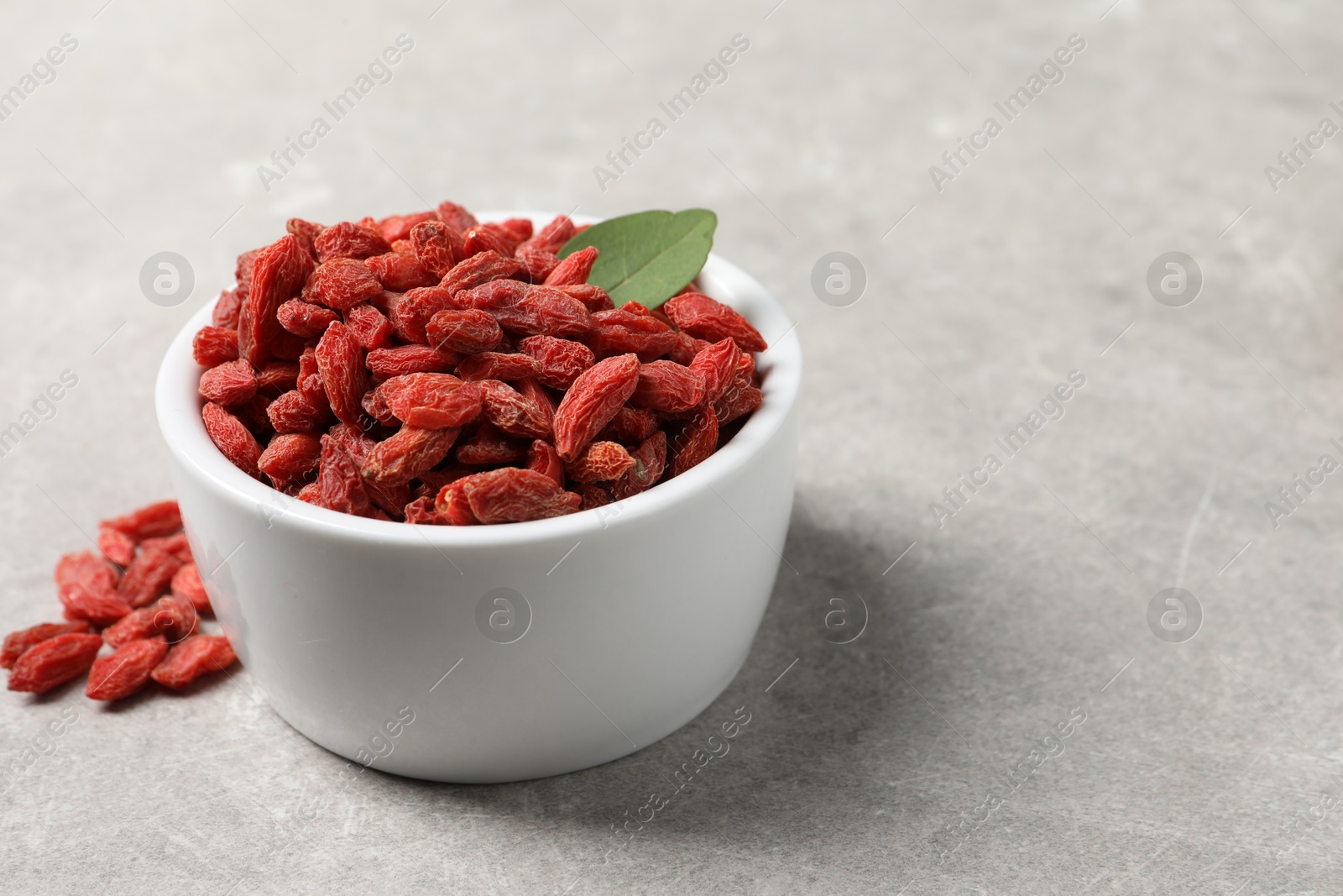 Photo of Dried goji berries and leaf in bowl on grey textured table, closeup. Space for text