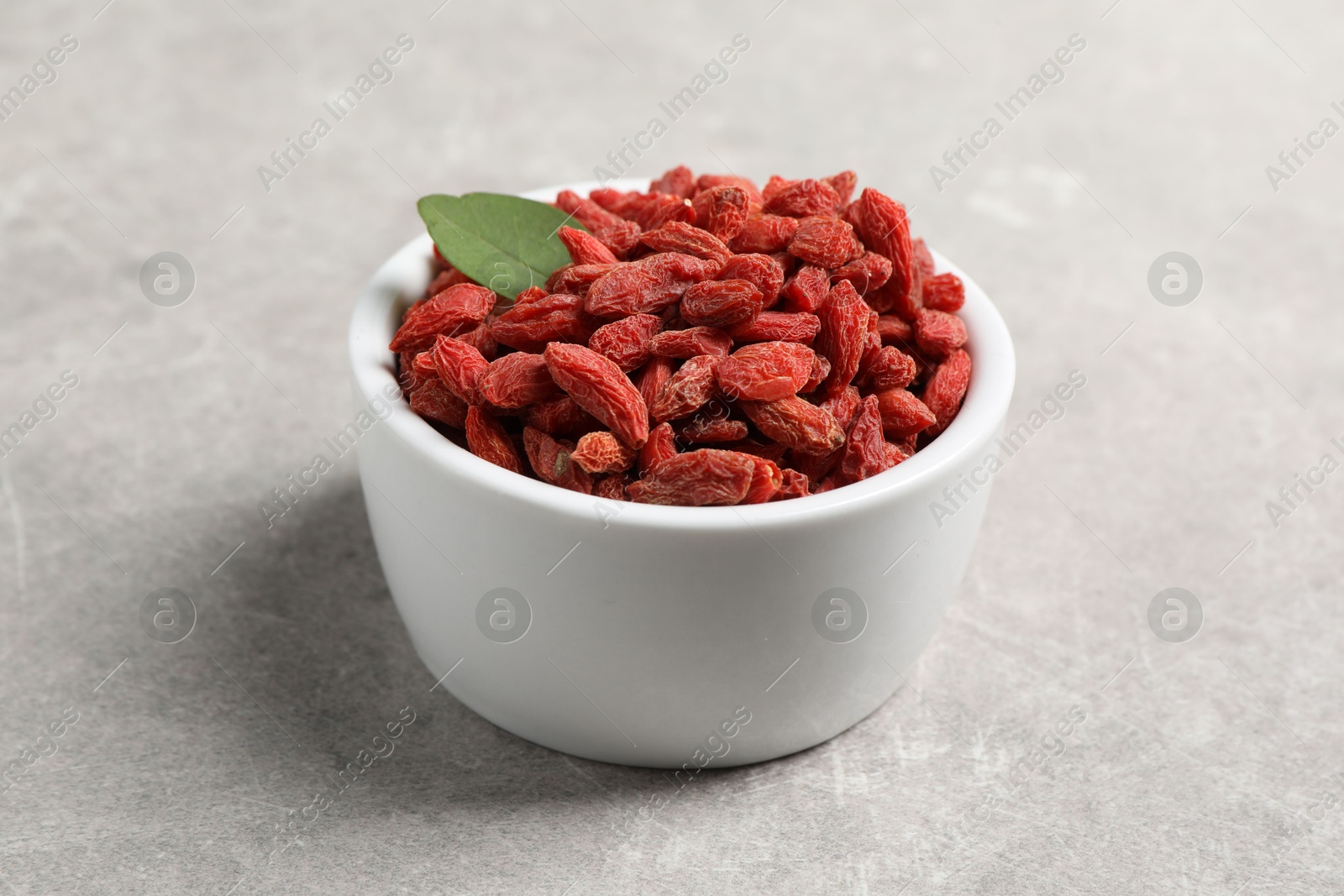 Photo of Dried goji berries and leaf in bowl on grey textured table, closeup