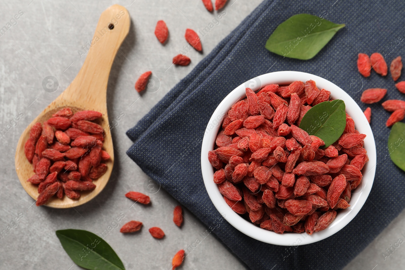 Photo of Dried goji berries and leaves on grey textured table, flat lay