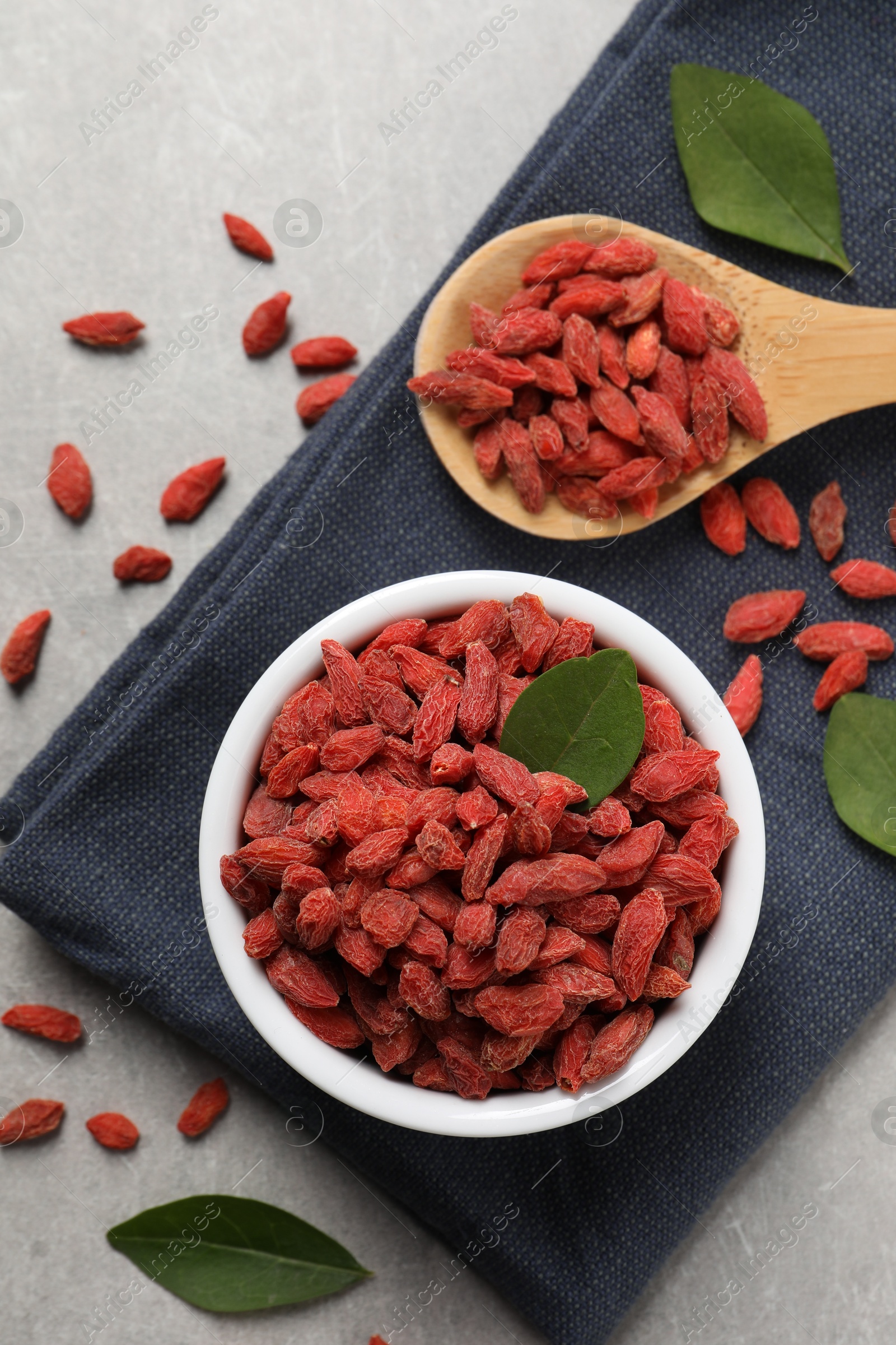 Photo of Dried goji berries and leaves on grey textured table, flat lay