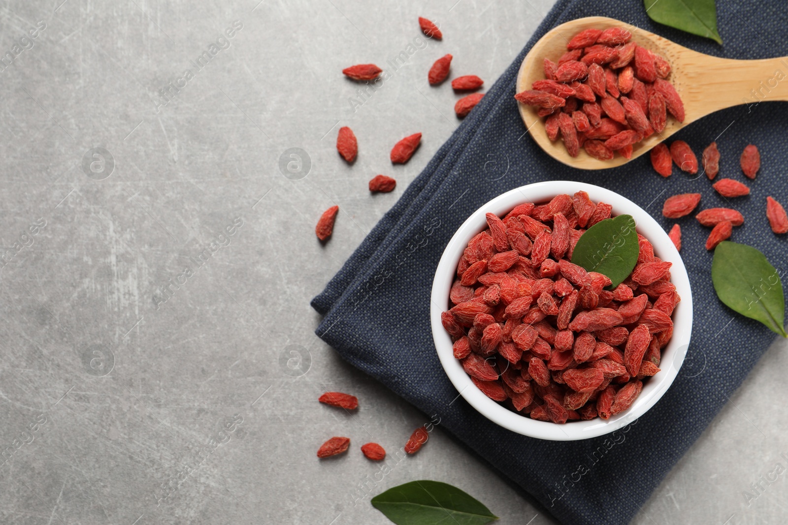 Photo of Dried goji berries and leaves on grey textured table, flat lay. Space for text