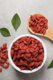 Dried goji berries and leaves on grey textured table, flat lay