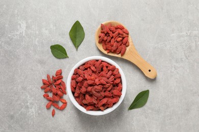 Dried goji berries and leaves on grey textured table, flat lay