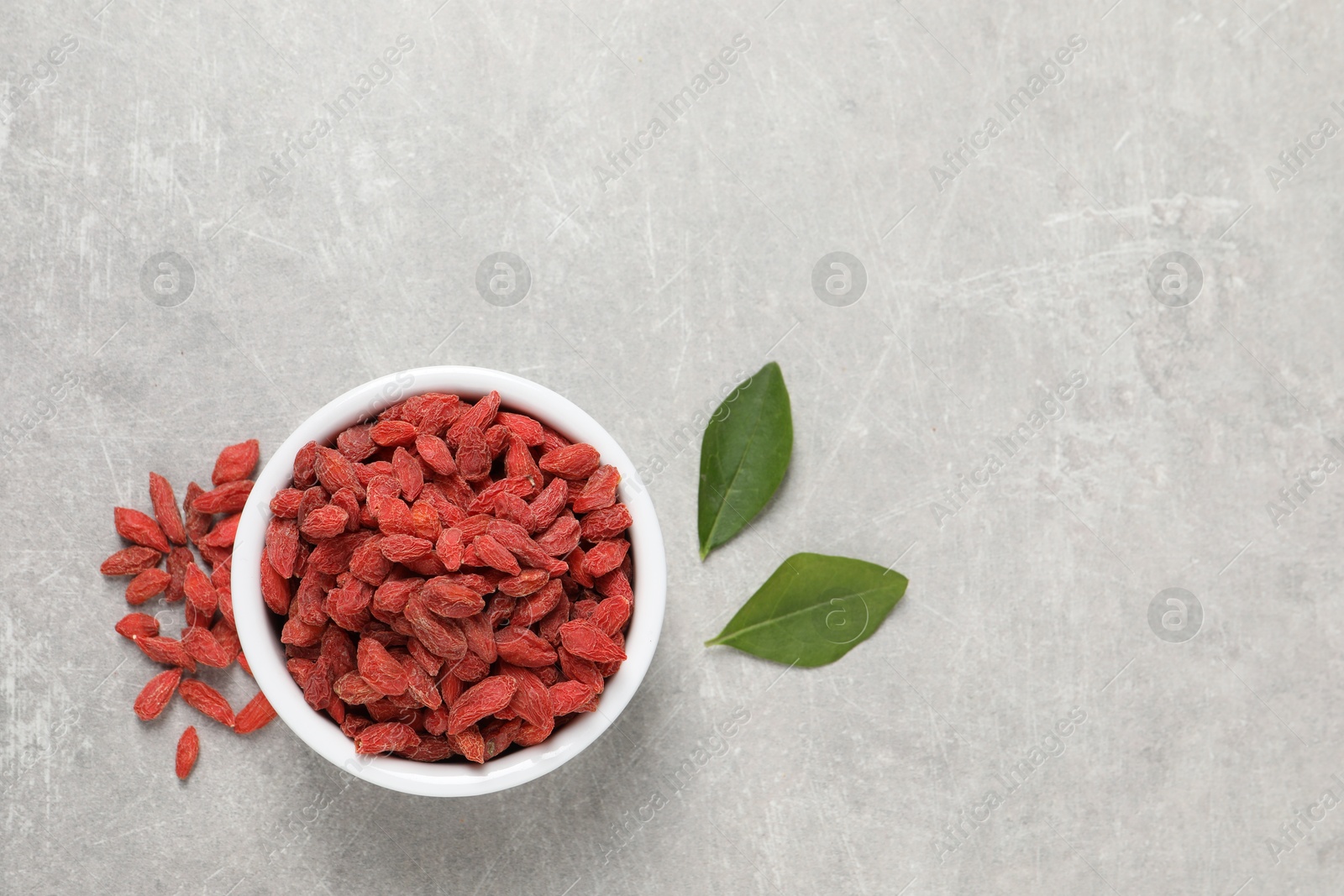 Photo of Dried goji berries and leaves on grey textured table, flat lay. Space for text