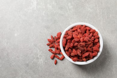 Dried goji berries in bowl on grey textured table, top view. Space for text