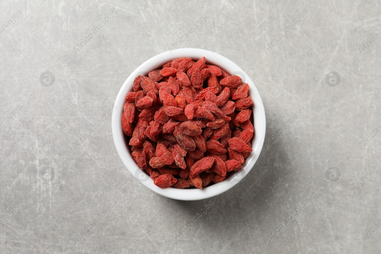 Photo of Dried goji berries in bowl on grey textured table, top view