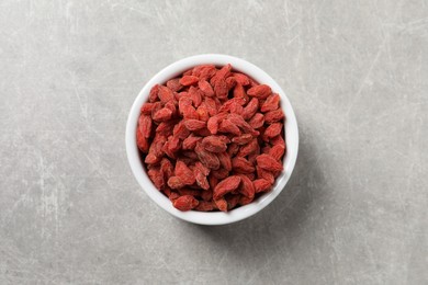 Dried goji berries in bowl on grey textured table, top view