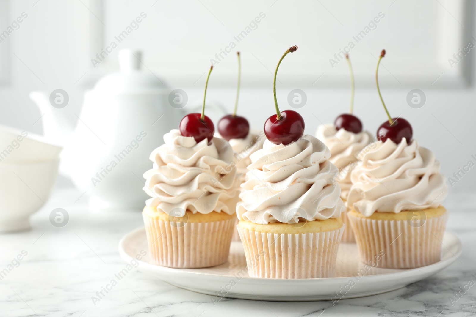 Photo of Delicious cupcakes with cream and cherries on white marble table