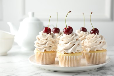 Delicious cupcakes with cream and cherries on white marble table