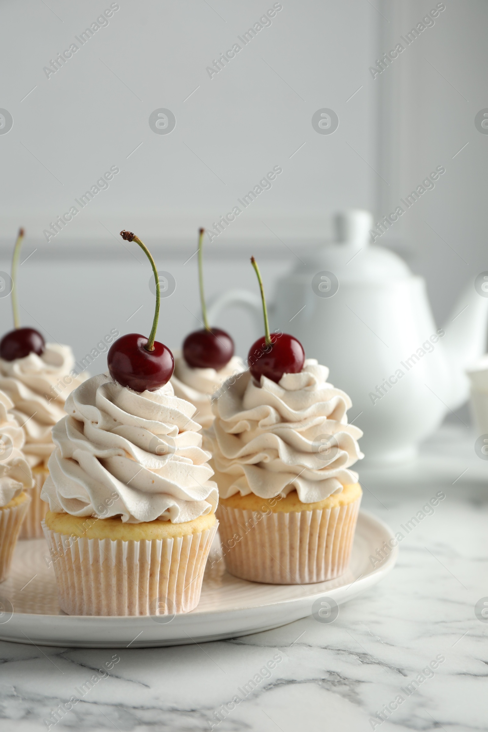 Photo of Delicious cupcakes with cream and cherries on white marble table