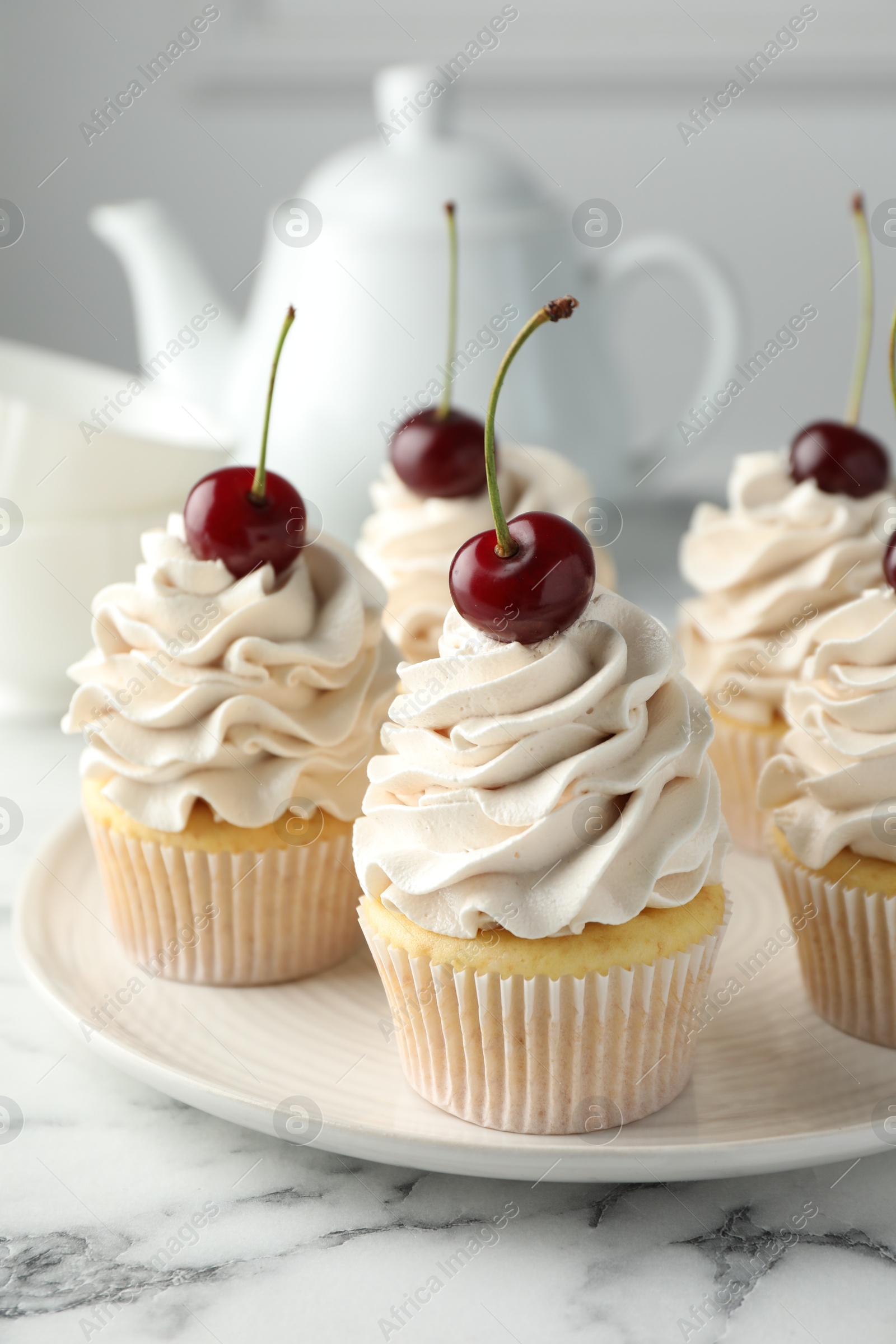 Photo of Delicious cupcakes with cream and cherries on white marble table