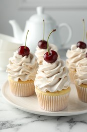 Photo of Delicious cupcakes with cream and cherries on white marble table