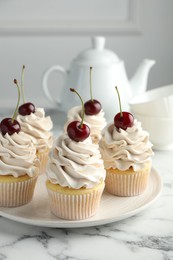 Photo of Delicious cupcakes with cream and cherries on white marble table