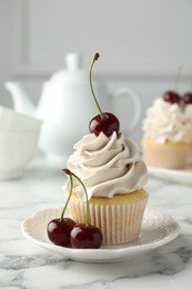 Delicious cupcake with cream and cherries on white marble table