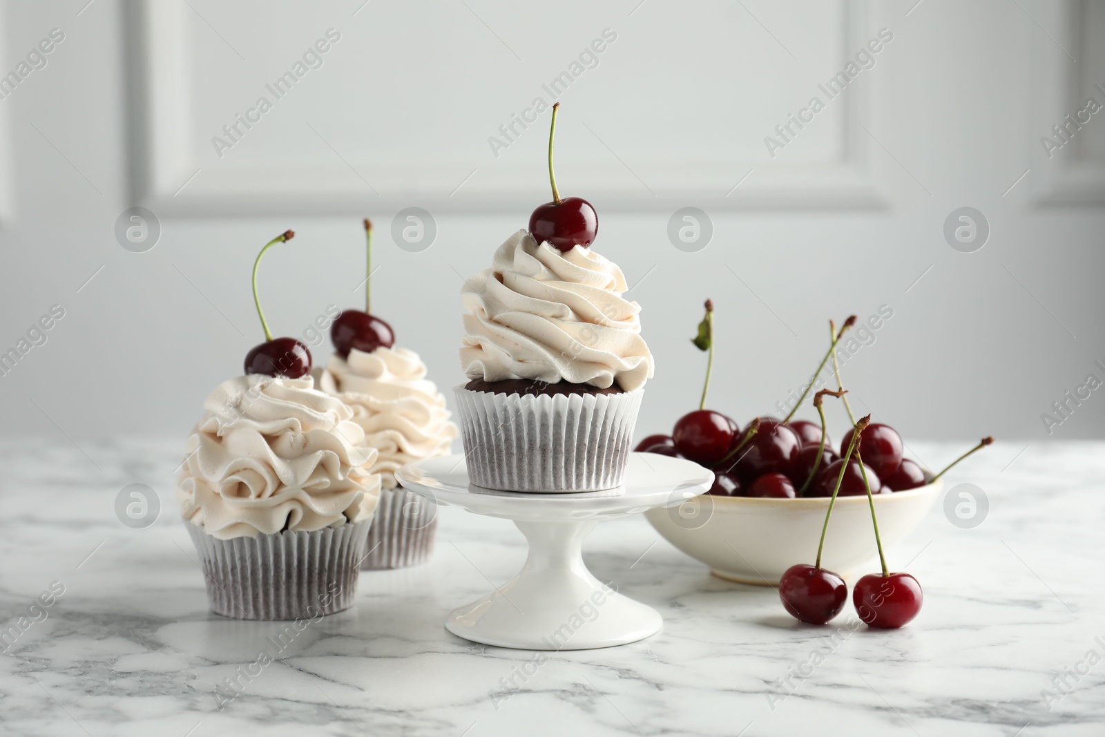 Photo of Delicious cupcakes with cream and cherries on white marble table