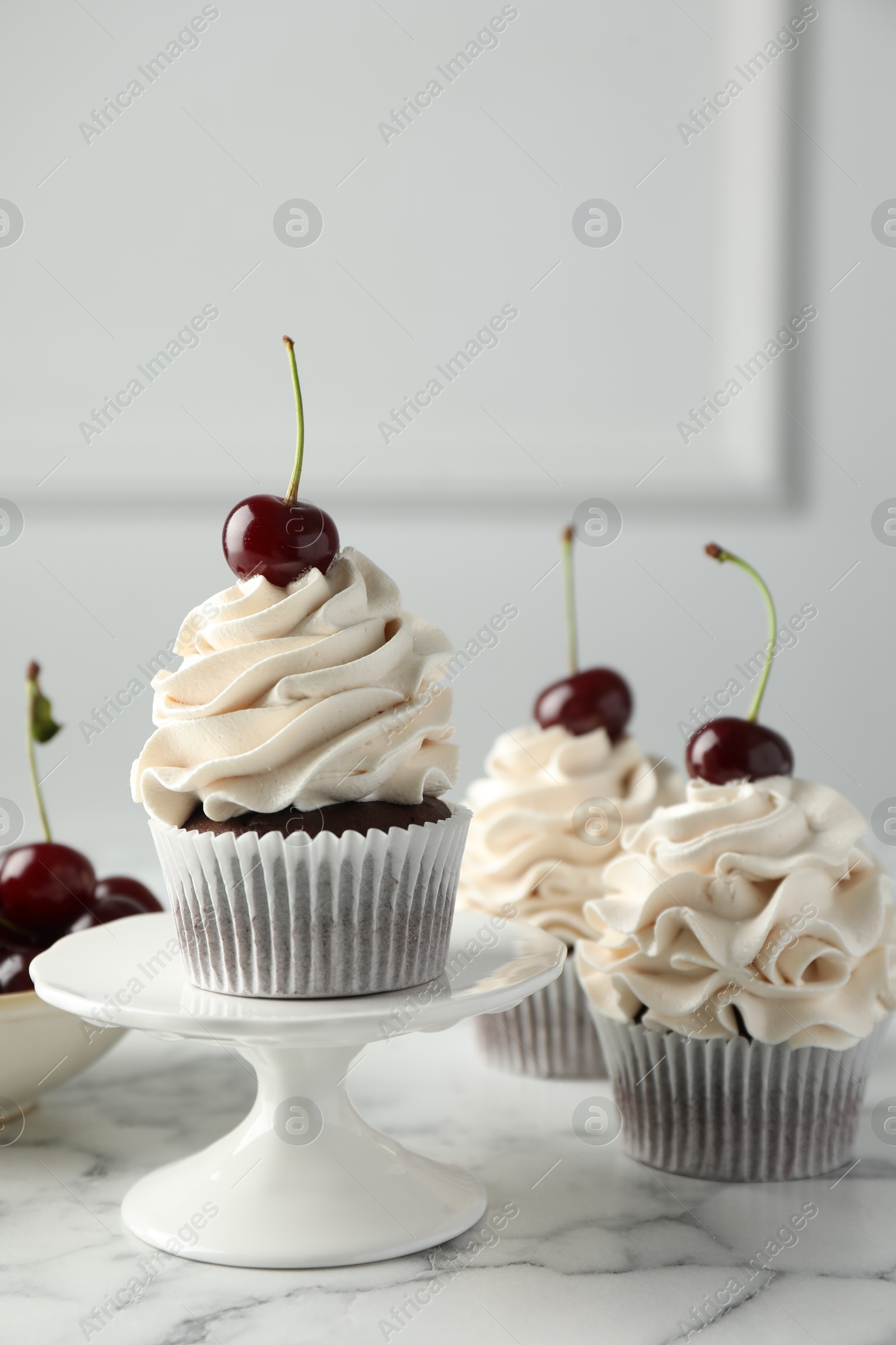 Photo of Delicious cupcakes with cream and cherries on white marble table