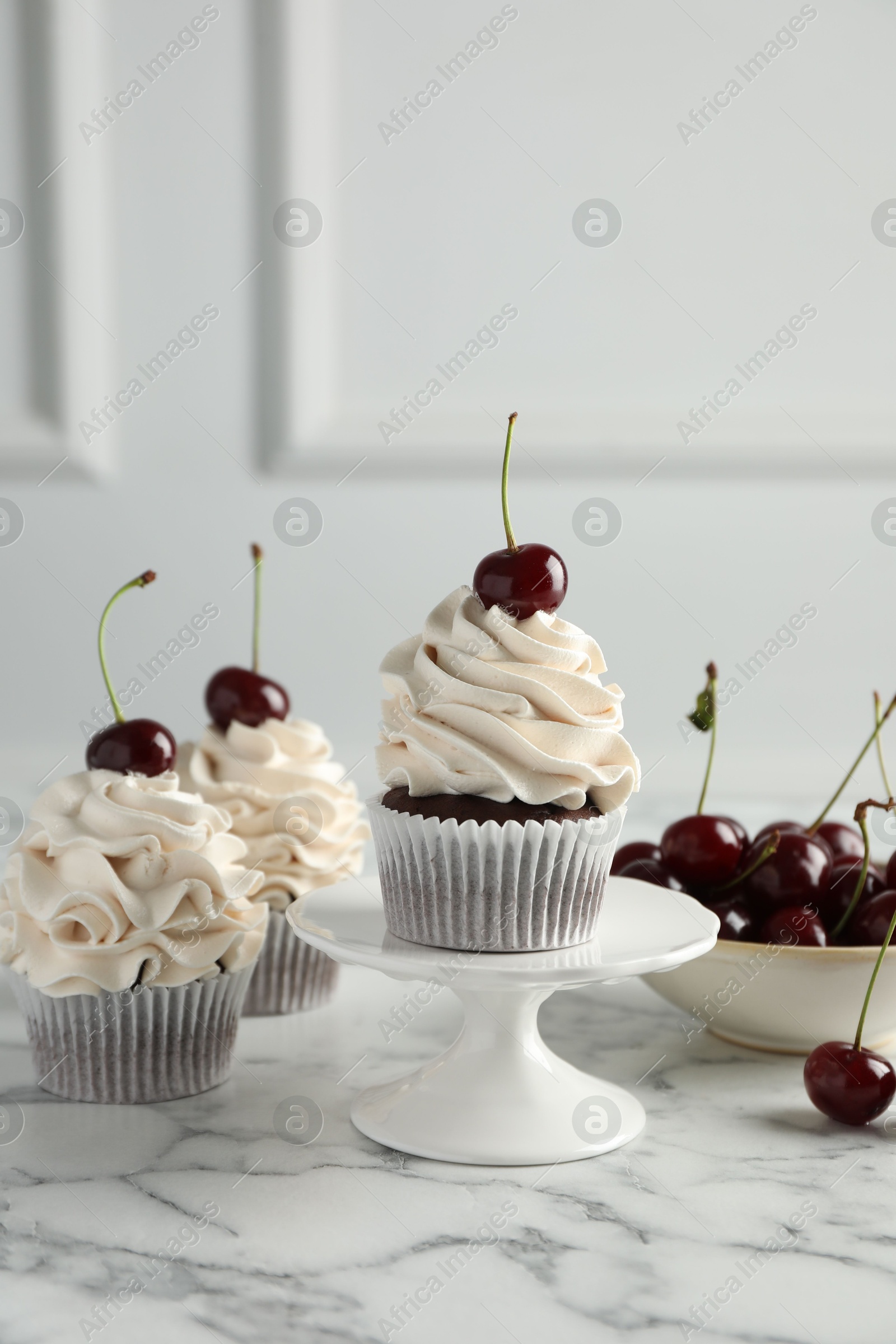 Photo of Delicious cupcakes with cream and cherries on white marble table