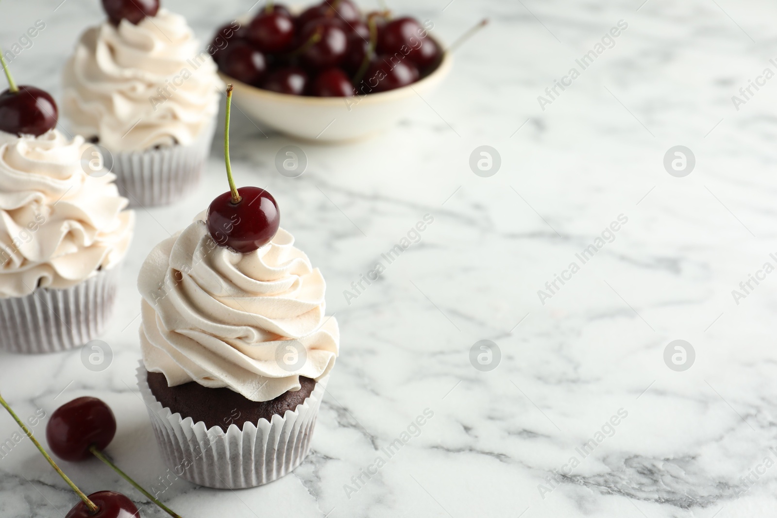 Photo of Delicious cupcakes with cream and cherries on white marble table, space for text