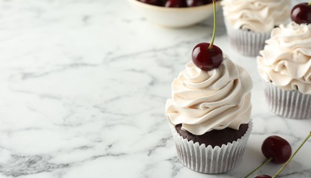 Delicious cupcakes with cream and cherries on white marble table, space for text