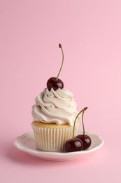 Delicious cupcake with cream and cherries on pink background