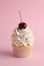 Delicious cupcake with cream and cherry on pink background