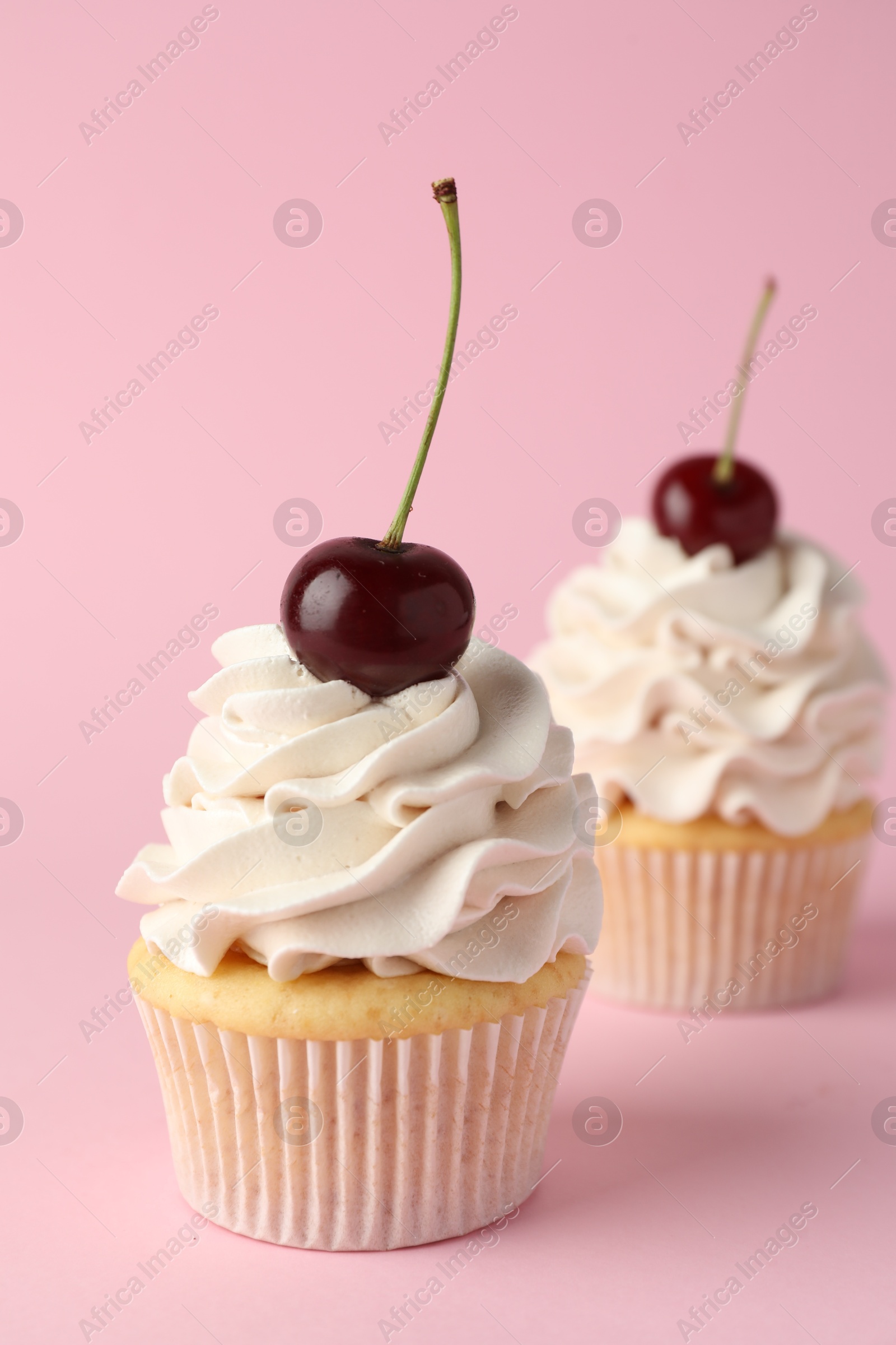 Photo of Delicious cupcakes with cream and cherries on pink background