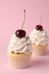 Delicious cupcakes with cream and cherries on pink background