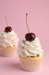 Delicious cupcakes with cream and cherries on pink background