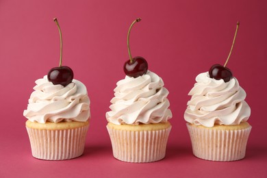 Delicious cupcakes with cream and cherries on red background