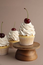 Delicious cupcakes with cream and cherries on dark beige background