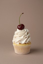 Photo of Delicious cupcake with cream and cherry on dark beige background