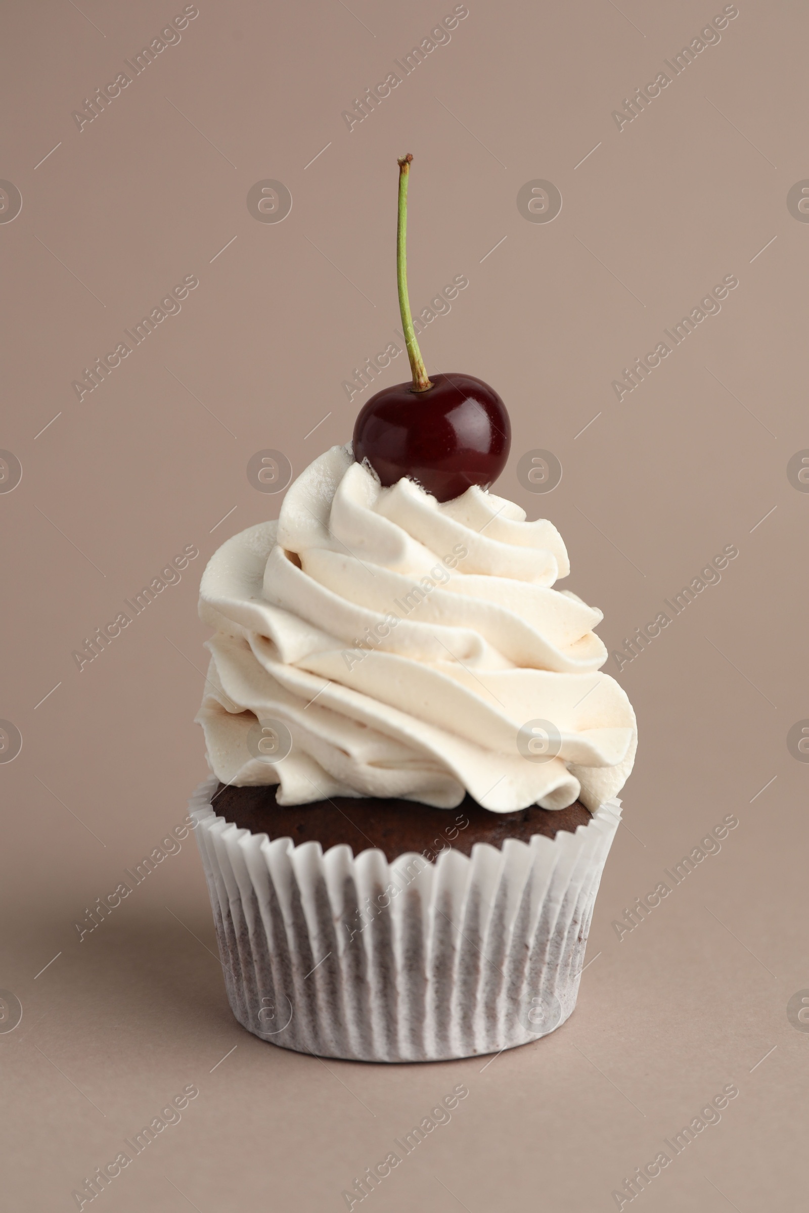 Photo of Delicious cupcake with cream and cherry on dark beige background