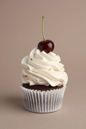 Photo of Delicious cupcake with cream and cherry on dark beige background