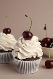 Photo of Delicious cupcakes with cream and cherries on dark beige background