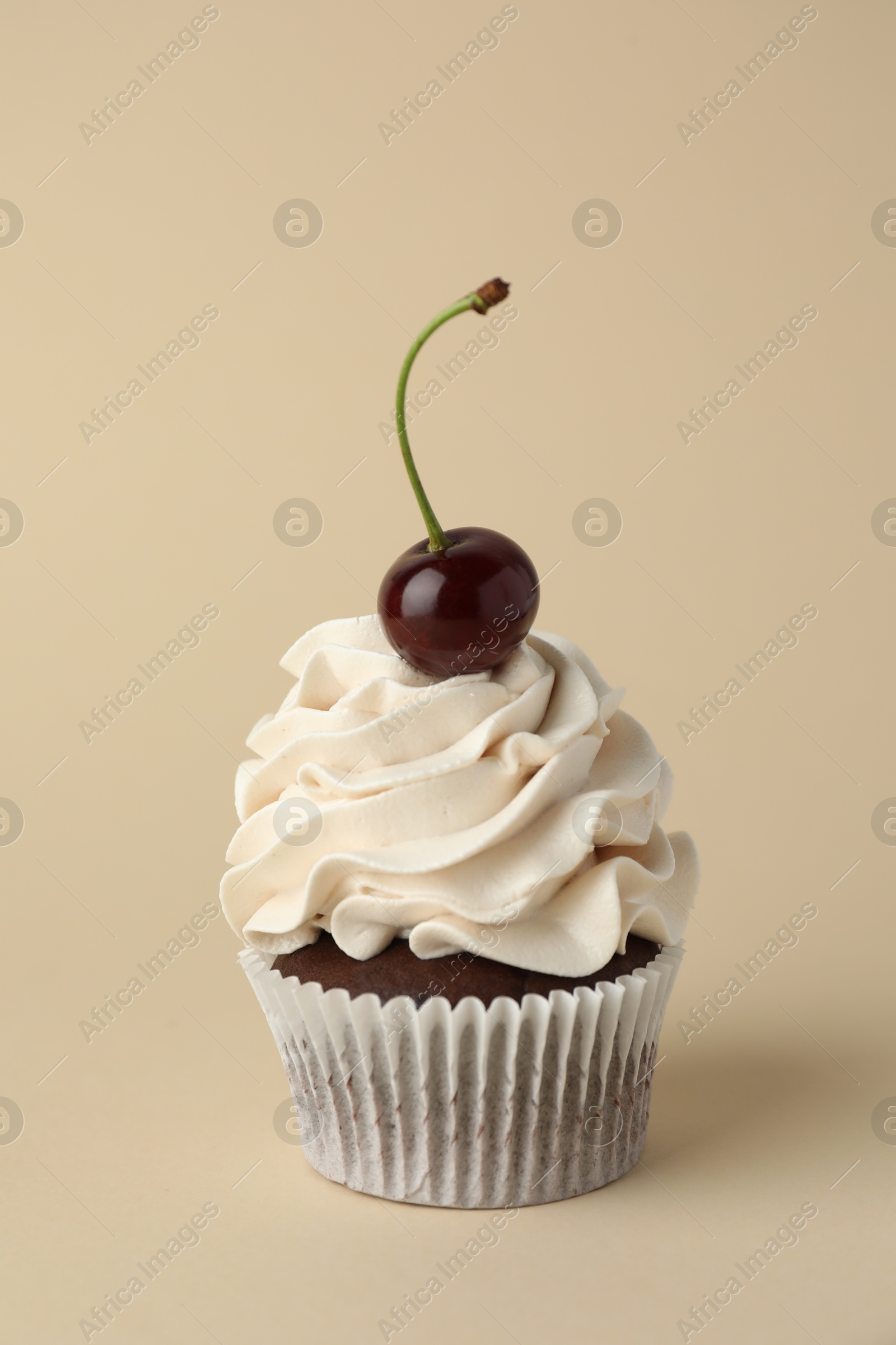 Photo of Delicious cupcake with cream and cherry on beige background