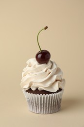 Delicious cupcake with cream and cherry on beige background