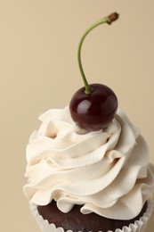 Photo of Delicious cupcake with cream and cherry on beige background, closeup