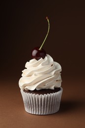 Photo of Delicious cupcake with cream and cherry on brown background