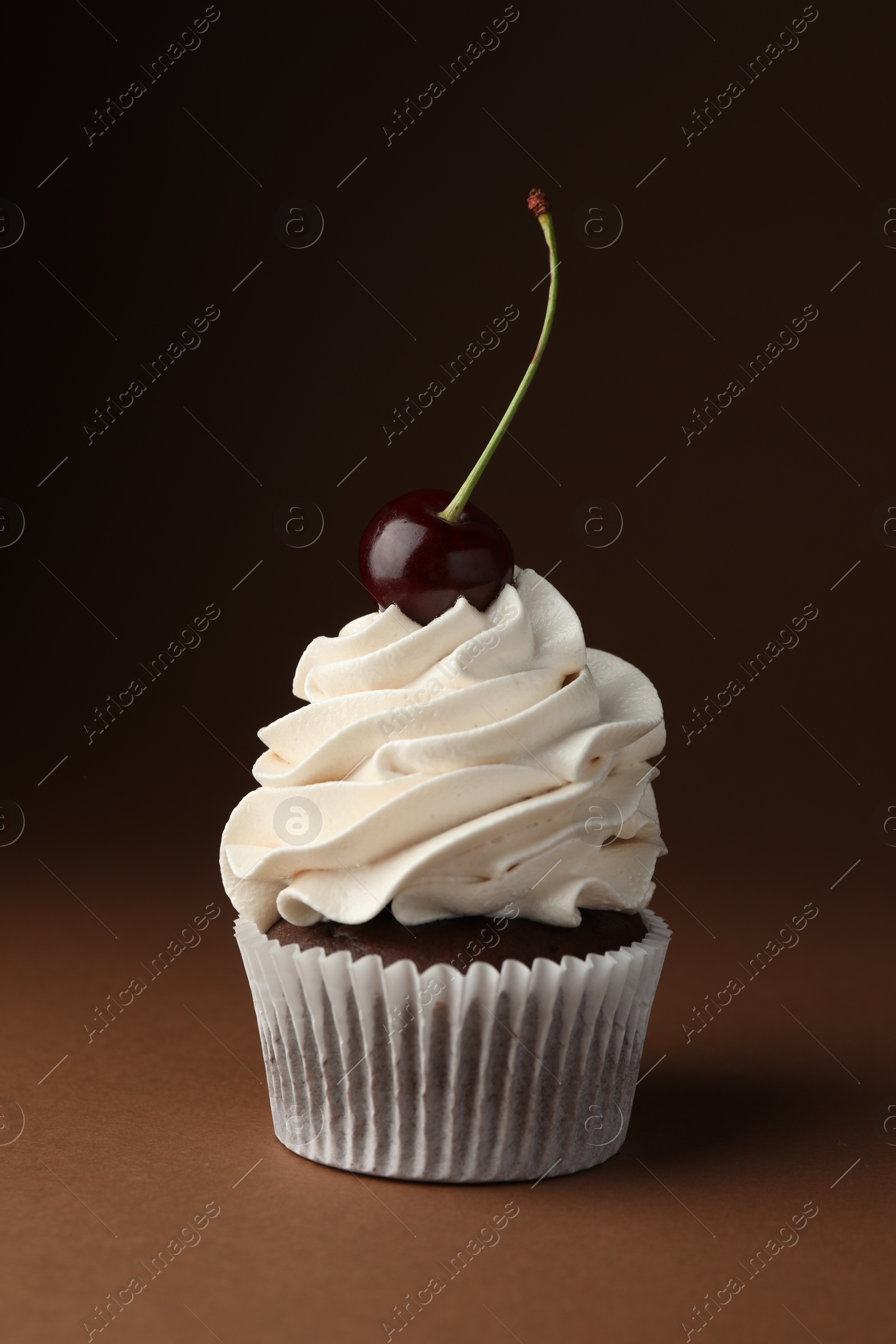 Photo of Delicious cupcake with cream and cherry on brown background