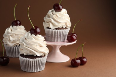 Photo of Delicious cupcakes with cream and cherries on brown background