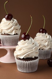 Photo of Delicious cupcakes with cream and cherries on brown background