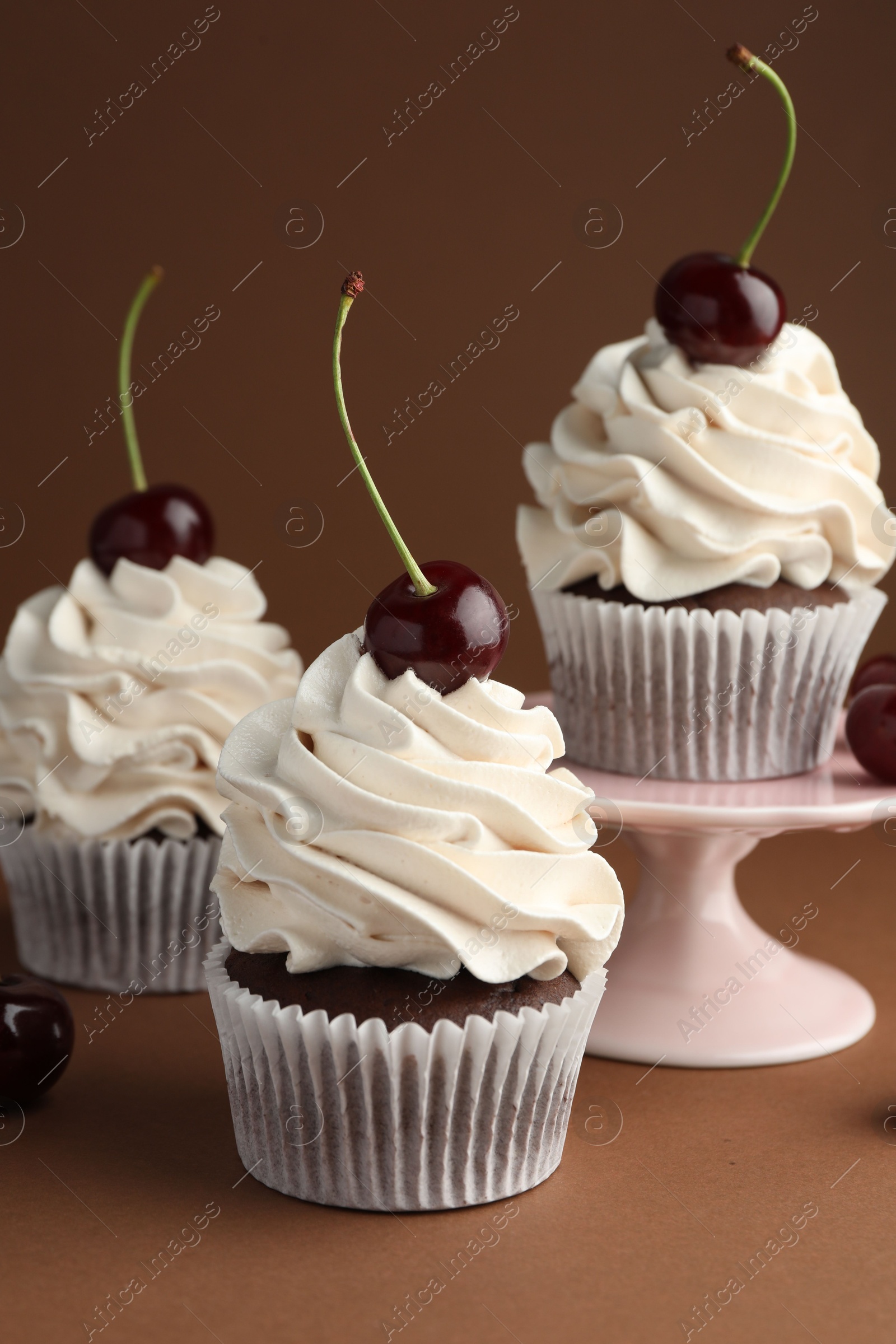 Photo of Delicious cupcakes with cream and cherries on brown background