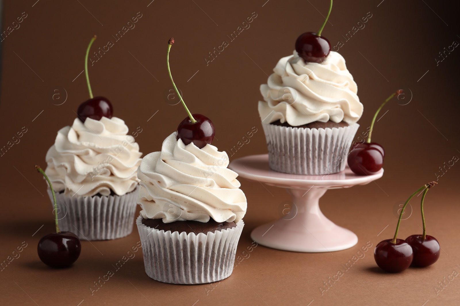 Photo of Delicious cupcakes with cream and cherries on brown background