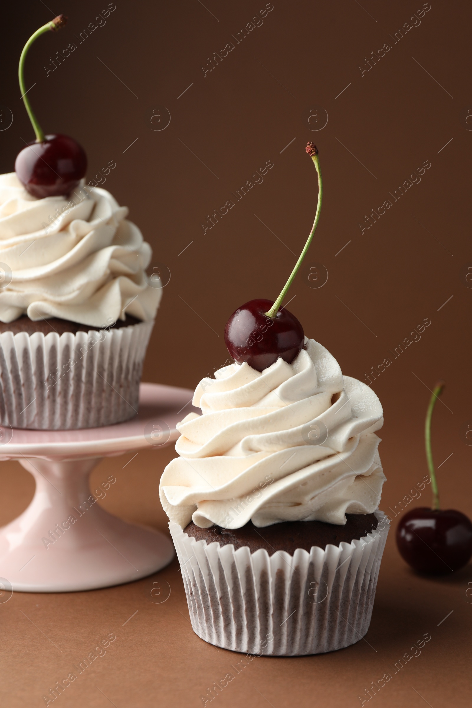 Photo of Delicious cupcakes with cream and cherries on brown background