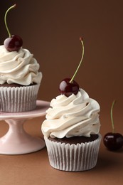 Photo of Delicious cupcakes with cream and cherries on brown background